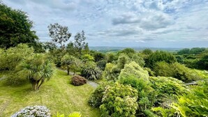 A lush garden with a variety of trees and shrubs, a clear sky, and a distant view of the landscape. - Chalet in Kent with Hot Tub & Countryside Views (Hoath)