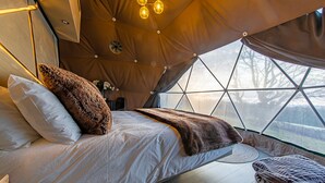 A cozy, modern tent-style bedroom with a large bed, a hanging light fixture, and a view through a geometric window. - Chalet in Kent with Hot Tub & Countryside Views (Hoath)