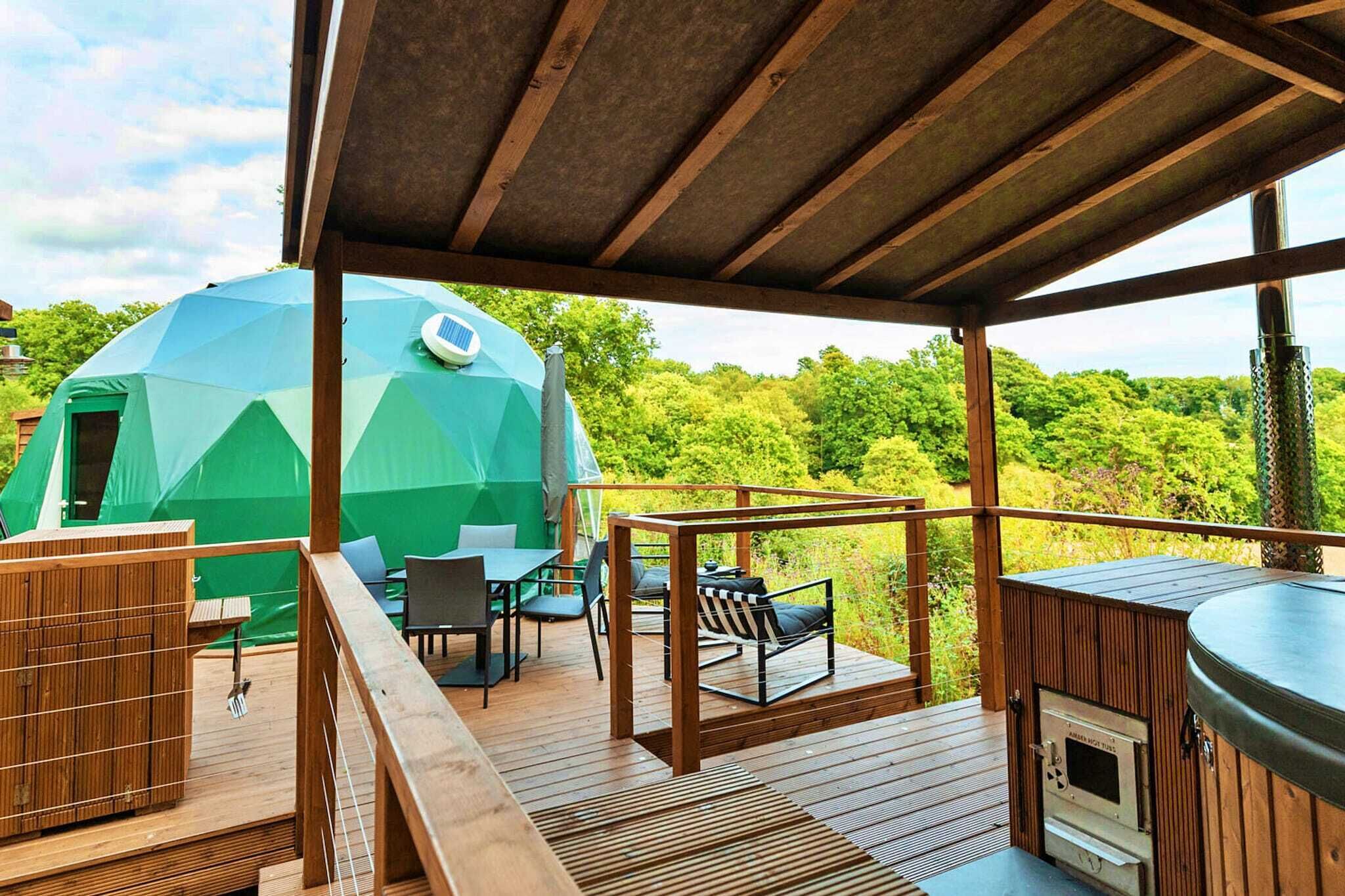 A wooden deck with a hot tub, a table with chairs, and a green geodesic dome tent.