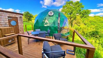 A wooden deck with a transparent dome structure, outdoor furniture, and a brick building.