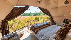 Un hébergement sous tente comprenant un lit, des rideaux et une vue sur l’extérieur.