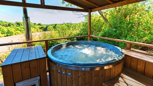 Un bain à remous sur une terrasse en bois, avec vue sur une zone boisée.