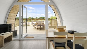 Una camera accogliente con un'ampia finestra ad arco, una TV a schermo piatto, mobili in legno e vista su una terrazza esterna con sedie e un tavolo.