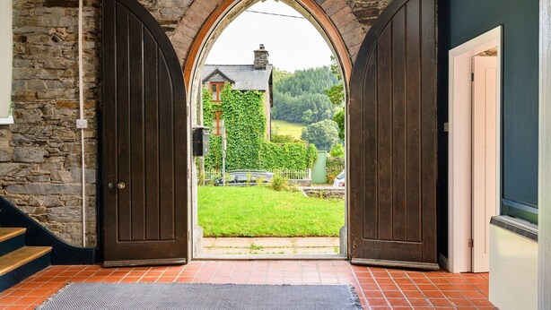 A stone wall, a wooden door, and a view of a house with a green lawn. - Chapel in Snowdonia with Hot Tub & Games Room (Dinas Mawddwy)