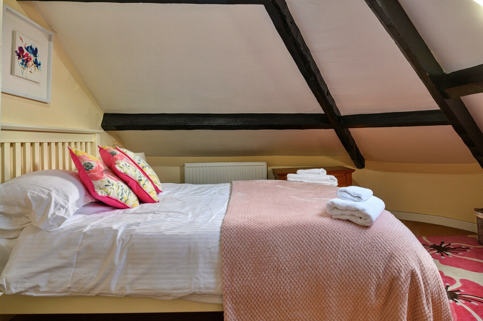 A bedroom with a sloped ceiling, a bed with white linens, a pink blanket, and a radiator.