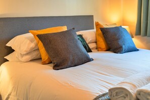 Een net opgemaakt bed met witte lakens en meerdere kussens in verschillende kleuren.