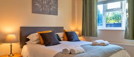 A neatly made bed with pillows, a bedside lamp, and a window with curtains.