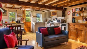Un salon chaleureux avec un canapé bleu et des meubles en bois, une cuisine avec des armoires blanches et une vue sur la verdure à l’extérieur.