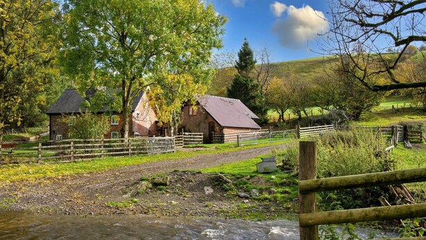 Un paysage rural avec une maison en pierre, une clôture en bois et un ruisseau.