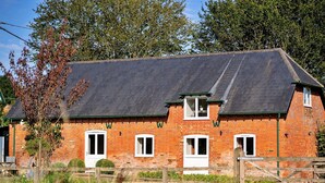 A brick building with a sloped roof, multiple windows, and a wooden fence in the foreground. - Holiday Home in Andover near New Forest Park (Barton Stacey)