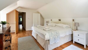 A bedroom with a large bed, a nightstand, a dresser, and a door leading to another room. - Holiday Home in Andover near New Forest Park (Barton Stacey)