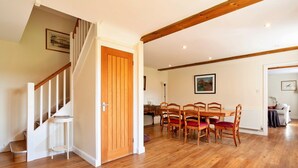 A spacious room with a wooden staircase, a dining area with wooden chairs, and a white radiator. - Holiday Home in Andover near New Forest Park (Barton Stacey)