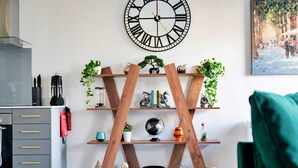 A modern living room with a wooden X-shaped shelf unit, a large wall clock, and a painting.