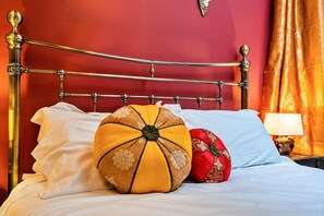 Un lit avec un cadre en métal, des oreillers blancs et des coussins décoratifs aux couleurs jaune et rouge.