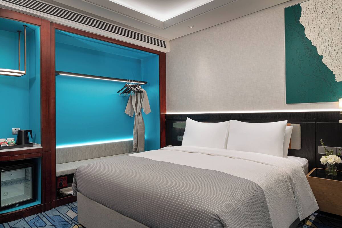 A modern hotel room with a large bed, a seating area with a coffee machine, and a wall-mounted TV.