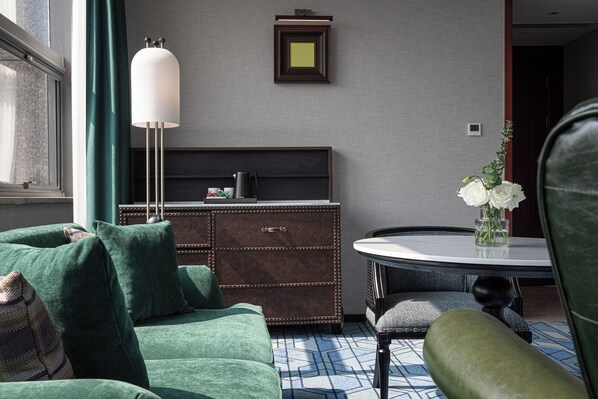 Un salón moderno con un sofá verde, una mesa redonda con un jarrón de flores y un mueble bajo de madera oscura.