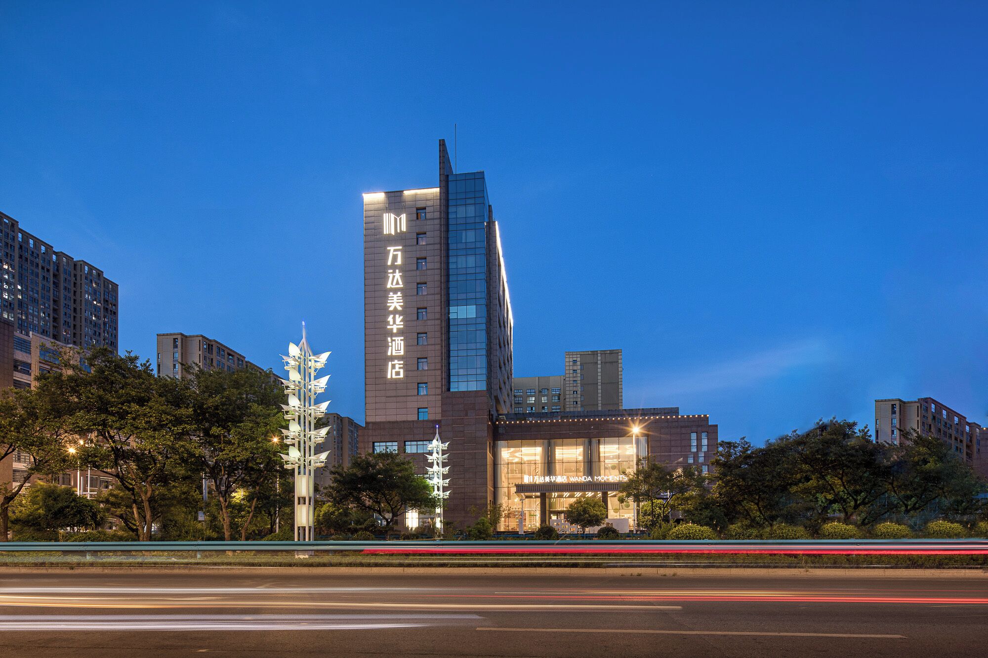 Um hotel moderno com um edifício alto e retangular, e uma estrutura mais baixa na frente.