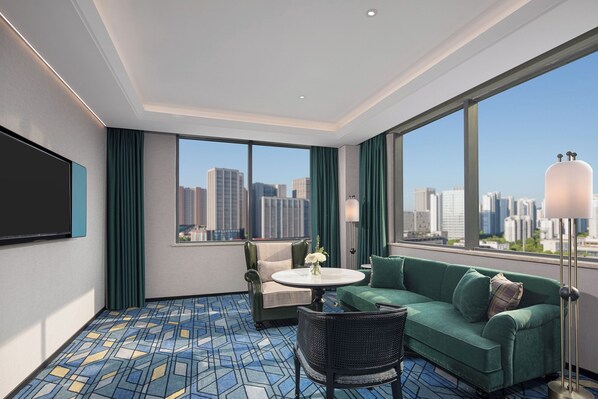 A modern hotel room with a large window offering a city view, a sofa, a chair, a small table, and a flat-screen TV. - Wanda Moments Hotel Suzhou Wuzhong (Suzhou)
