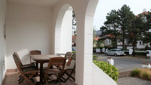 Un'area salotto all'aperto coperta con tavolo e sedie, un muro bianco e vista sulla strada e sugli edifici sullo sfondo.
