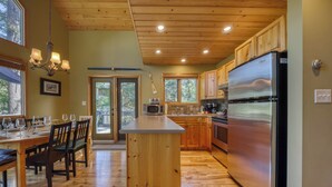A spacious kitchen with wooden cabinets, a large stainless steel refrigerator, and a dining area with a wooden table and chairs. - Sable Pine Cabin | Sleeps 8 | Nature Trails | Wood Stove (Area F (Columbia Lake/Windermere Lake))