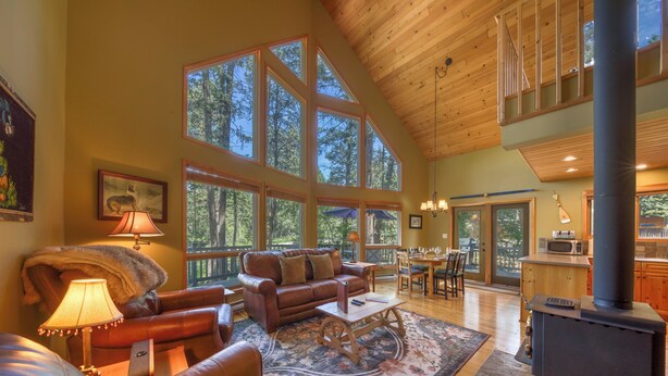 A spacious living room with a large window, a fireplace, and a cozy seating area. - Sable Pine Cabin | Sleeps 8 | Nature Trails | Wood Stove (Area F (Columbia Lake/Windermere Lake))