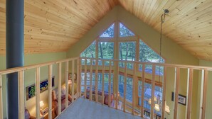 A loft bedroom with a sloped ceiling, large windows, and a view of the outdoors. - Sable Pine Cabin | Sleeps 8 | Nature Trails | Wood Stove (Area F (Columbia Lake/Windermere Lake))