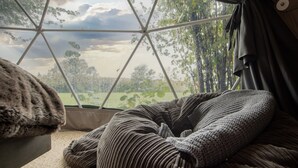 A cozy room with a large window, a cushioned seating area, and a view of trees and sky. - Chalet in Kent with Hot Tub & Countryside Views (Hoath)