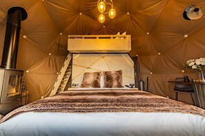 Cozy tent-style room with a central bed and a lofted bunk, a compact stove, and a charming geometric light fixture.