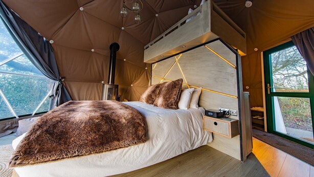 A tent-style bedroom with a bed, wooden headboard, and a window with a view of trees. - Chalet in Kent with Hot Tub & Countryside Views (Hoath)