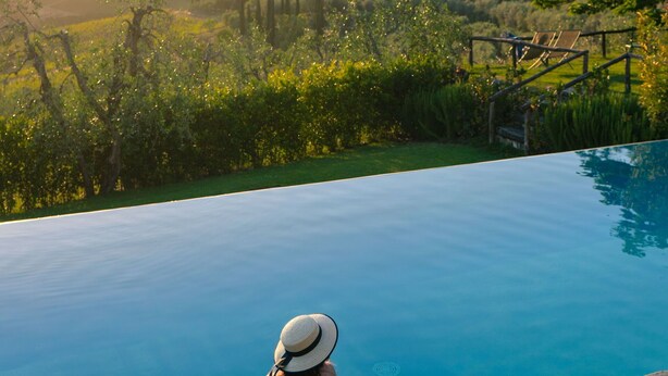 A woman sitting by a pool with a view of a mountainous landscape.
