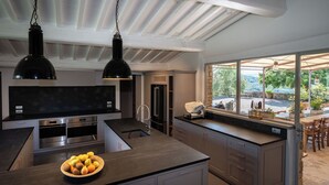 A modern kitchen with a large island, stainless steel appliances, and a view of the outdoors through a large window.