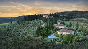 A villa surrounded by olive groves and cypress trees, with a pool and a view of the surrounding hills.
