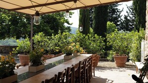 An outdoor dining area with terracotta planters, wooden chairs, and hanging light fixtures.