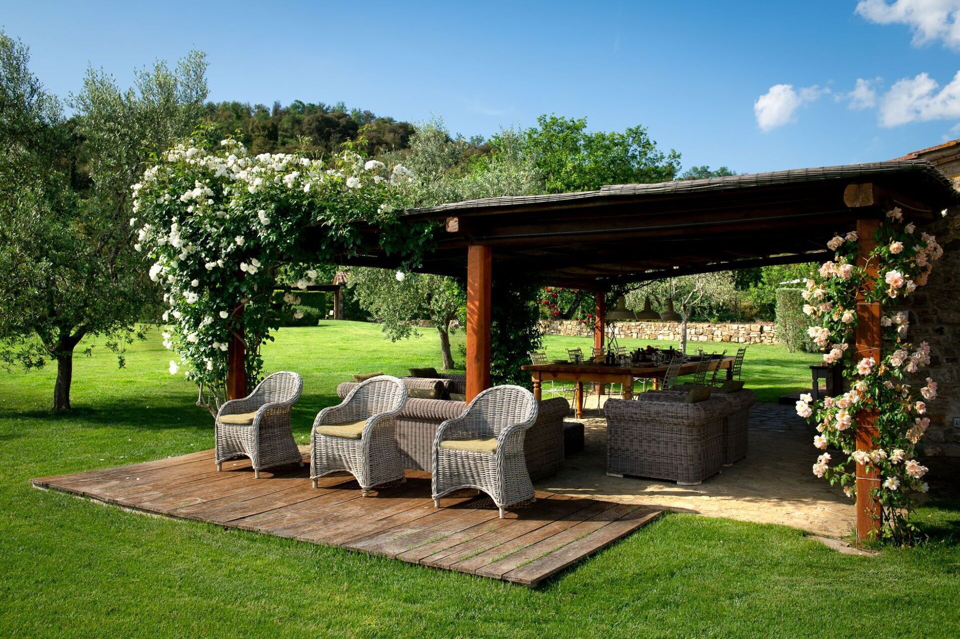 Un espace extérieur aménagé en terrasse, avec des meubles en osier et une pergola recouverte de rosiers grimpants.