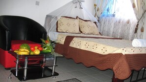 A bedroom with a bed, a chair, a table with fruit, and a window with curtains. - Alcazar Hotel Kisumu (Kisumu)