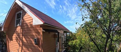 Une petite maison en bois d’un seul étage, avec un toit rouge, une petite fenêtre et un boîtier électrique apparent.