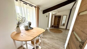 Una habitación con una mesa de madera, un armario blanco y un ventanal con cortinas.
