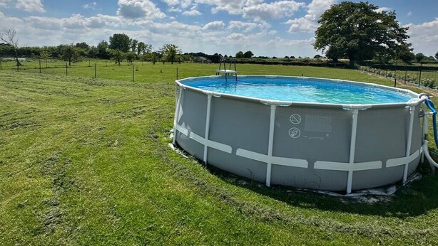 Una piscina elevada circular en un campo cubierto de césped, con un árbol al fondo.