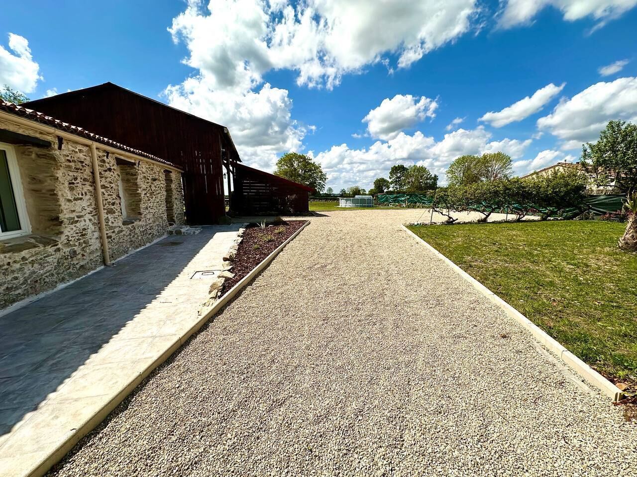 A gravel path leading to a rustic stone building with a wooden roof.