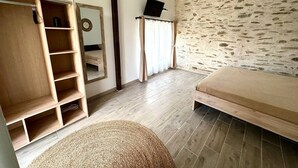 Un dormitorio con una cama, un armario de madera, un espejo y una pared de piedra.