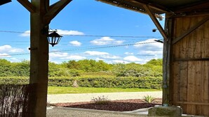 Un espacio al aire libre cubierto con una estructura de madera, un farol y vistas a un jardín ajardinado y una carretera.