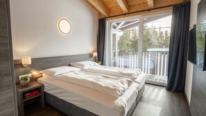 A bedroom with a bed, bedside tables, a lamp, and a view of the outdoors.