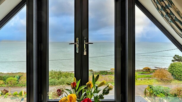 Blick aus einem Zimmer mit großem Fenster auf ein Gewässer, mit einer Tür im Vordergrund und einer Pflanze auf dem Fensterbrett.