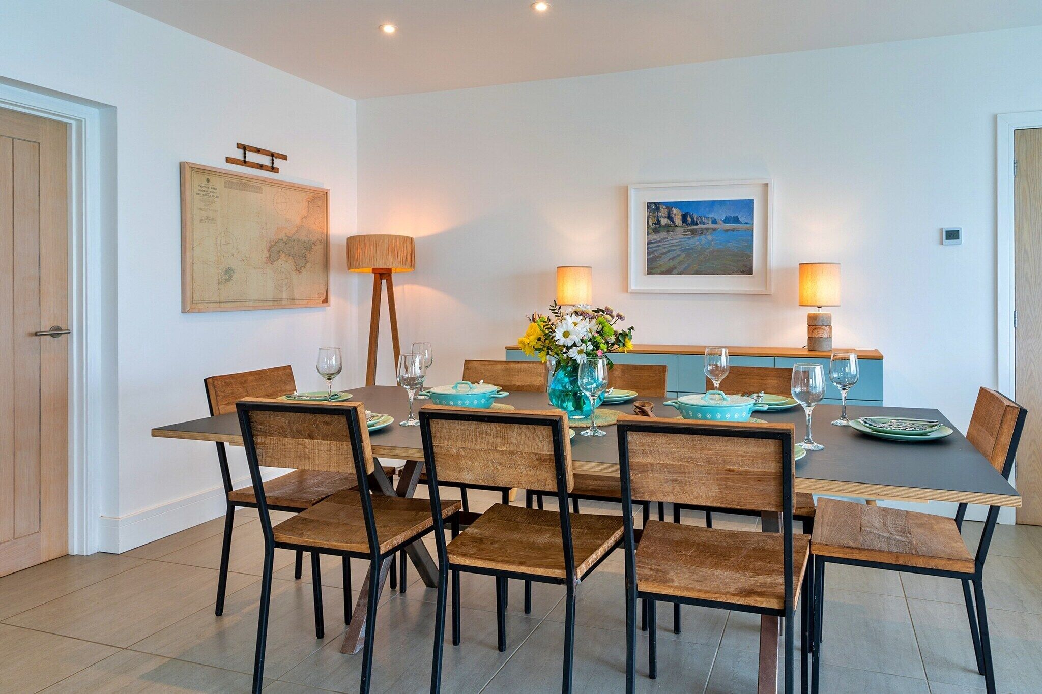 Un coin repas comprenant une table rectangulaire, six chaises en bois, deux lampadaires et un vase avec des fleurs.