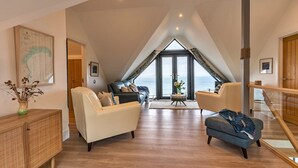 Ein geräumiger Loft mit hoher Decke, einem großen Fenster mit Meerblick und einem modernen Interieur mit Ledersofas und Holzboden.