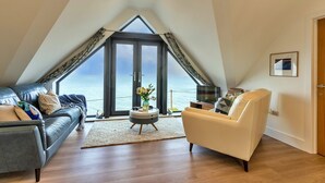 Ein modernes Schlafzimmer im Loft-Stil mit einem großen Dachfenster, einer gemütlichen Sitzecke mit Sofa und Sessel sowie Blick auf das Meer.
