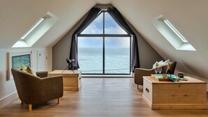 Ein modernes Schlafzimmer im Loft-Stil mit großem Dachfenster, Meerblick und einer gemütlichen Sitzecke mit einer Holzkommode.