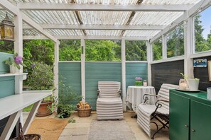 Un espacio de patio techado con una silla acolchada, una mesita y un armario.