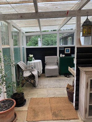 A conservatory with a table and chairs, a potted plant, a wicker basket, and a small cabinet.