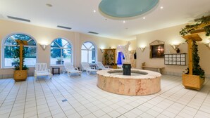 A spacious indoor area with a central circular marble fountain, white lounge chairs, and large windows providing natural light. - Appartement im Panoramic Hotel Bad Lauterberg (Bad Lauterberg)
